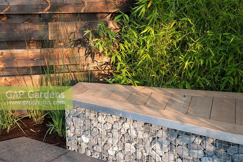 Basalt stone patio and basalt cobbles in cage - gambion wall with redwood timber top, seating and planting of bamboo Phyllostachys aurea 