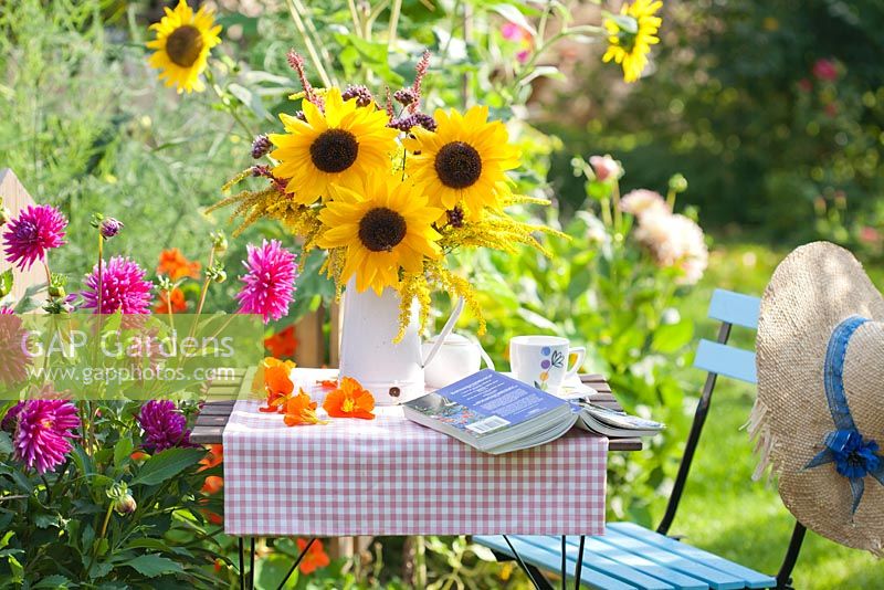 Bouquet of sunflowers and perennials Persicaria, Verbena bonariensis and Solidago in enamel jug in summer garden.