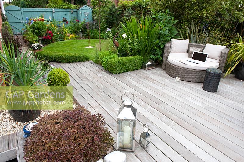 Contemporary hard wood Ipe deck with contrasting texture of the rounded pebbles. Planting includes Pittosporum tenuifolium 'Tom Thumb' and low Buxus sempervirens hedging leading to circular lawn with a back ground of cottage garden planting