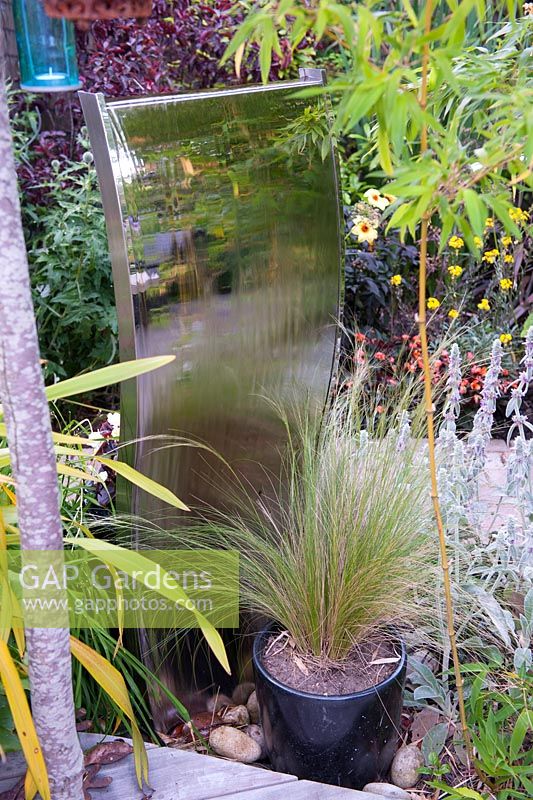Wavy stainless steel water feature mirror with Stipa tenuissima in black glazed pot
