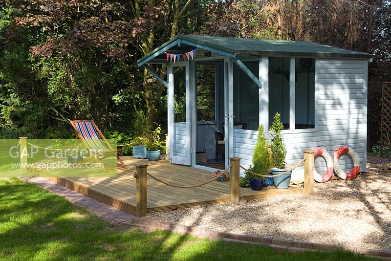 A Summer House and decking with a nautical theme surrounded by gravel. 