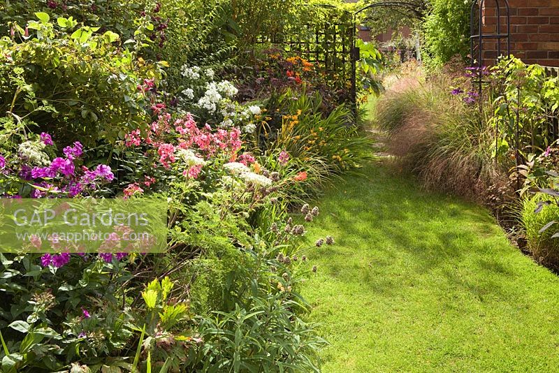 Path to the Bottom Garden Archway. Flowers include various Phlox, Allium sphaerocephalon and Selinum wallichianum. Stipa arundinacea lines the pathway on the right. Lincolnshire. August 2014. Summer.