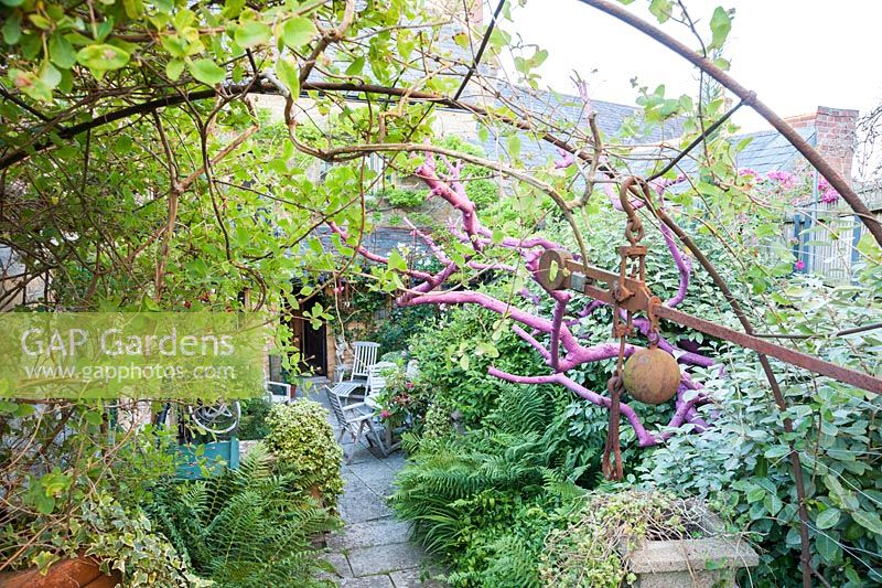 A dead tree, painted bright pink and draped with pieces of rusty metal, frames a sheltered courtyard with seating. 
