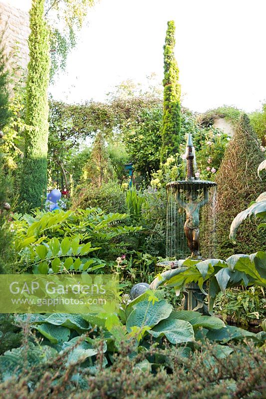 A fountain surrounded by strongly shaped foliage plants including hostas, Solomon's Seal, clipped lonicera and cardoons in a courtyard garden.