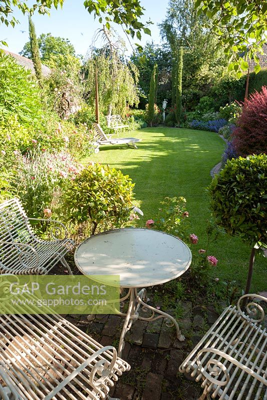 Seating area surrounded by clipped bays, with lawn, borders and pencil cypresses beyond. 