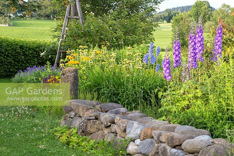 Granite stone wall and pillar around perennial border with delphiniums