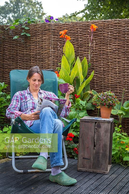 Woman reading a magazine, relaxing in her garden retreat