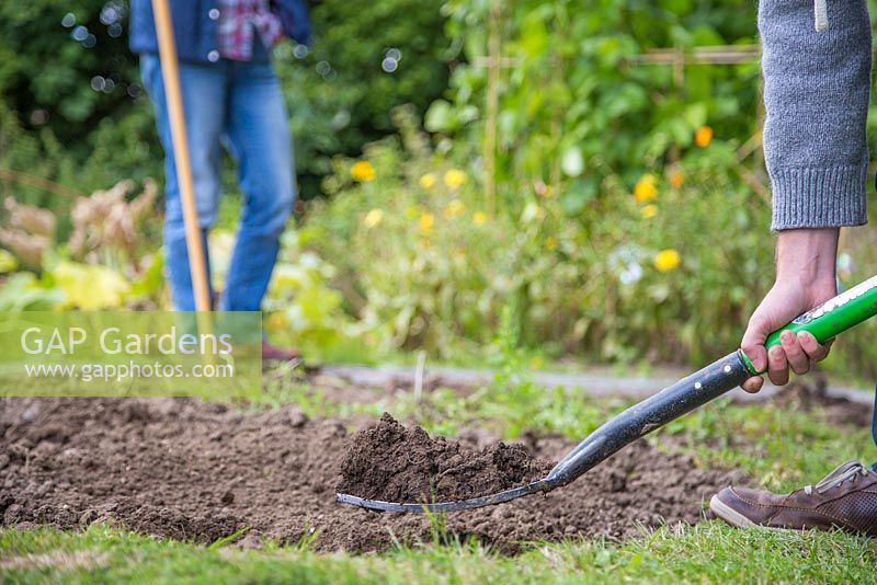 Man forking soil over in an alloment plot, woman standing watching in the background