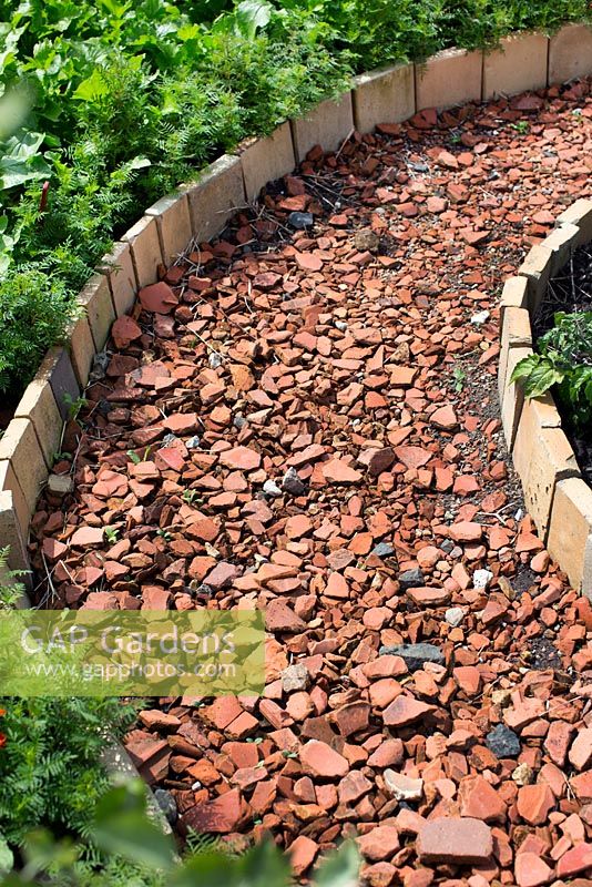 Path made from broken terracotta bordered with terracotta tiles in allotment garden