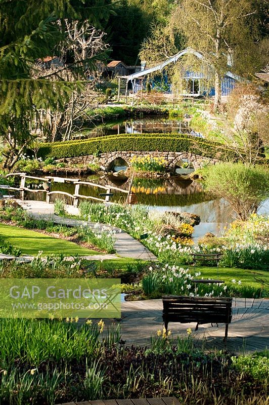 Garden view in springtime with seat bench, litte lake, bridge and garden house