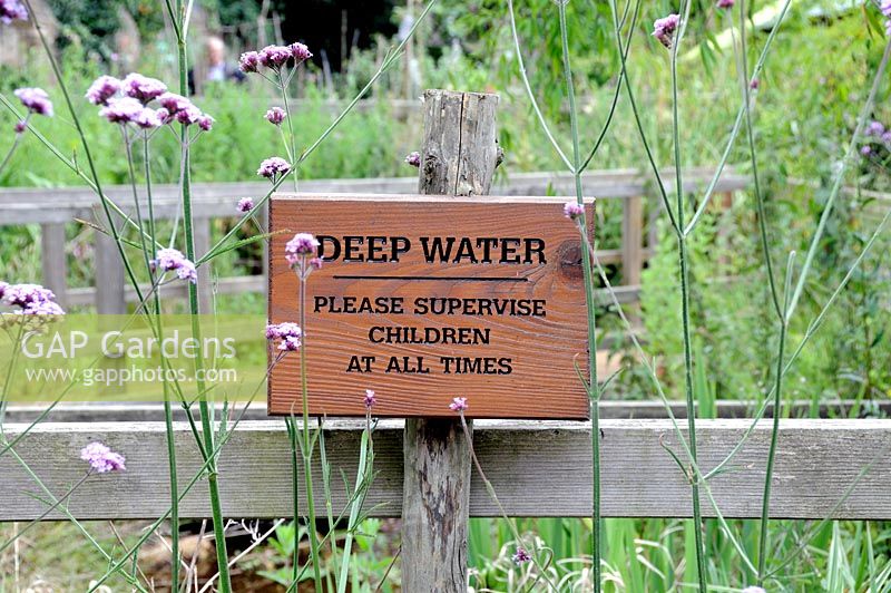 Deep Water warning sign in front of pond with Verbena bonariensis flowering around it, King Henrys Walk Garden, London Borough of Islington