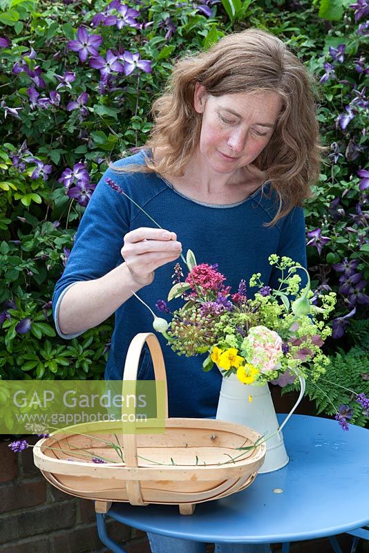 Lady making up floral display in garden using various cut blooms