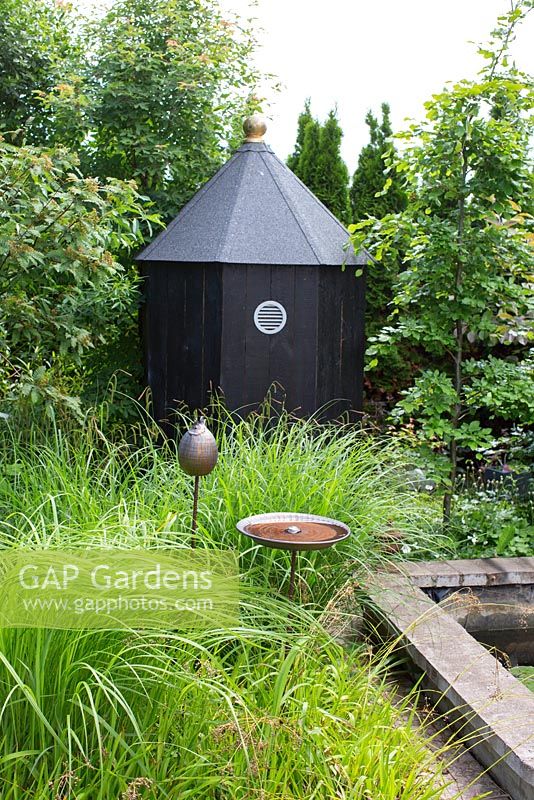 Octagonal wooden shed in garden, tall grass with birdbath, 