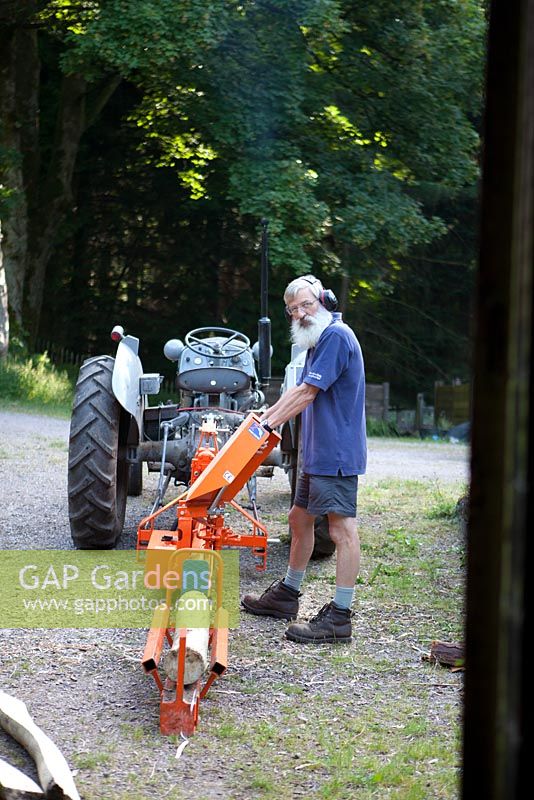Man feeding a wood splitter to make fire wood with tractor to tow