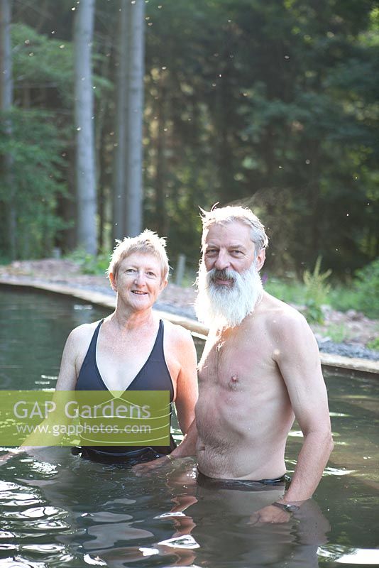 Couple standing in their natural swimming pond and the forest beyond - Sue and Ian Mabberley 