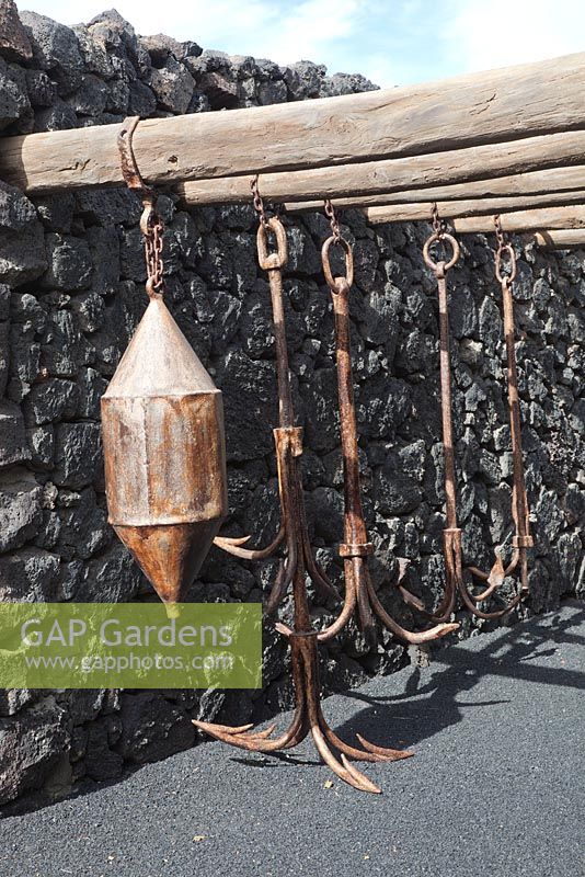 Agricultural metal found objects used as hanging sculpture on wooden poles in black volcanic rock garden