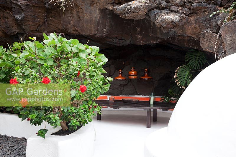 Part white washed black volcanic rock garden room in lava bubble with red flowering Pelargonium in planting pocket. Coffee table and ceramic lights circa 1960 1970.