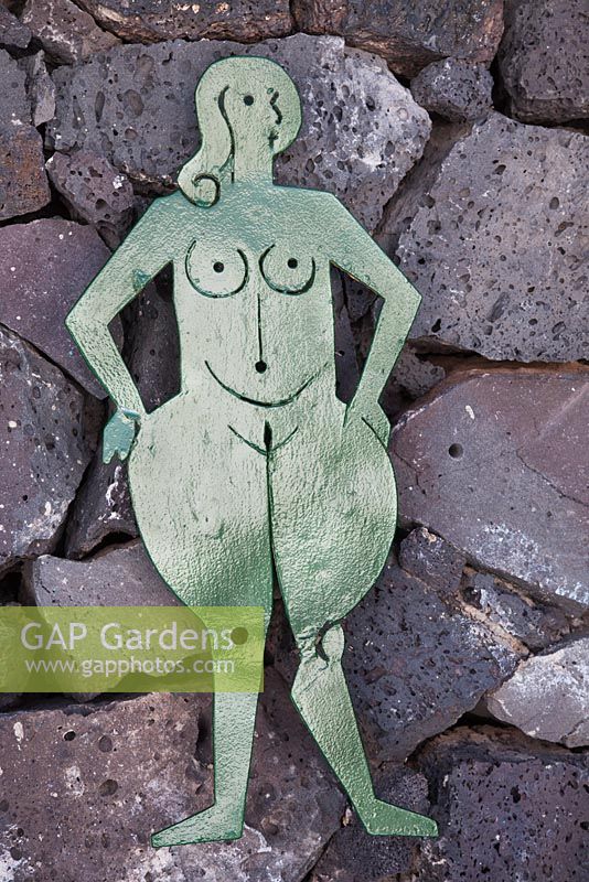 Green painted female metal figure for public toilet in garden on black volcanic rock wall