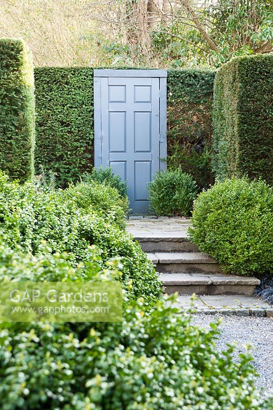 A false door framed by domes of loosely clipped box set into a yew 'wall' in a formal garden. 