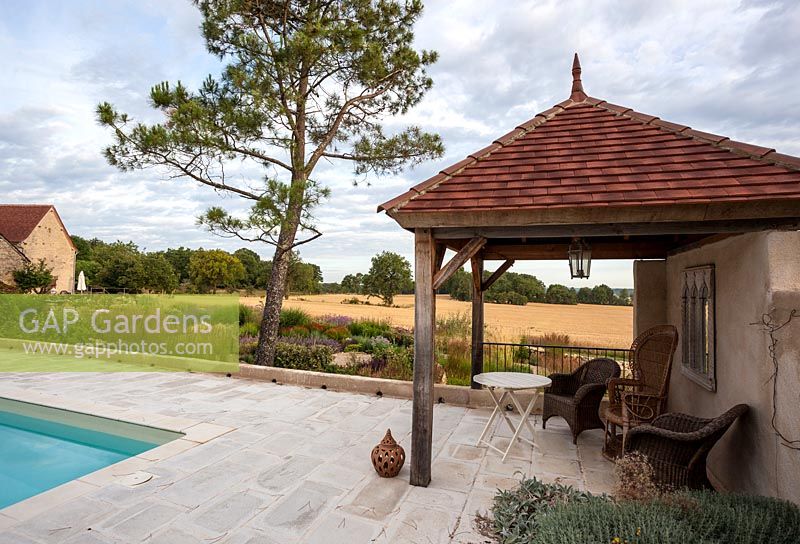 Poolside pavilion with wicker chairs and view onto garden with naturalistic planting and open fields