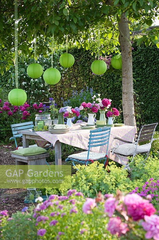 Garden Party in early summer under a walnut tree. Table with Paeonia - peony and lanterns