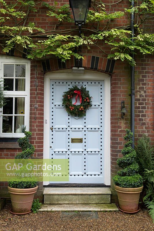 Lovely old front door decorated with a  traditional, long lasting Christmas wreath made using spruce, with red rose hips, dried pumpkins and ribbon. 