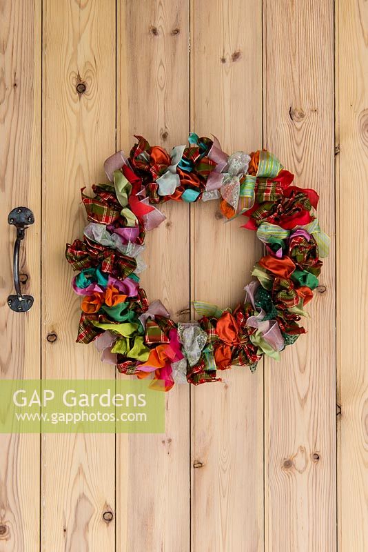 Colourful Christmas wreath made with ribbon. A wire wreath frame is wrapped 48 lengths of ribbon, each 45cm long, and in 8 different designs that are repeated, and tied in bows.