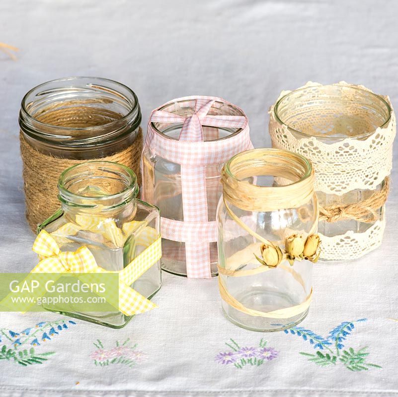 Decorating glass jars for garden posies step by step: A selection of glass jars decorated with gingham ribbon, gardener's jute twine string, cotton lace, rafia and dried rose buds.