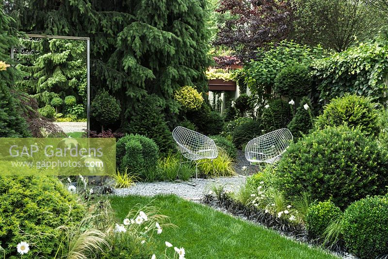 View of the mirror, modern wrought armchairs, sphere stainless steel water feature with LED lights and the path leading to the roof garden. Picea omorika, topiary: Taxus baccata and clipped Buxus sempervirens. 