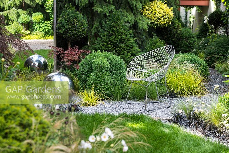 View of the mirror, modern wrought armchair, sphere stainless steel water feature with LED lights and the path leading to the roof garden. Picea omorika, topiary - Taxus baccata and Buxus sempervirens 