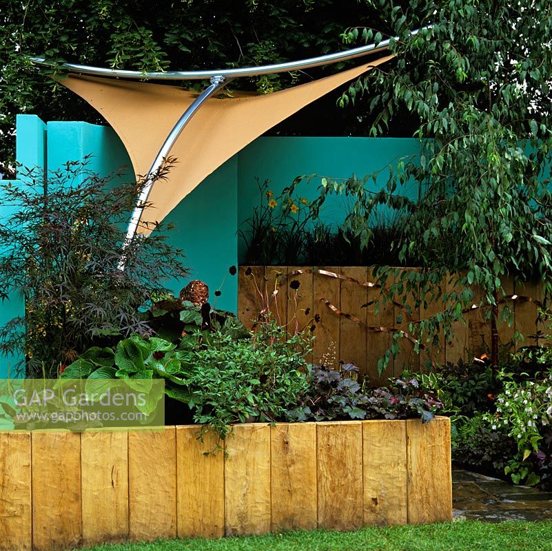 Buff coloured canvas awning suspended from stainless steel frame creates shade in a small, modern courtyard. Walls painted in blue create unusual backdrop.