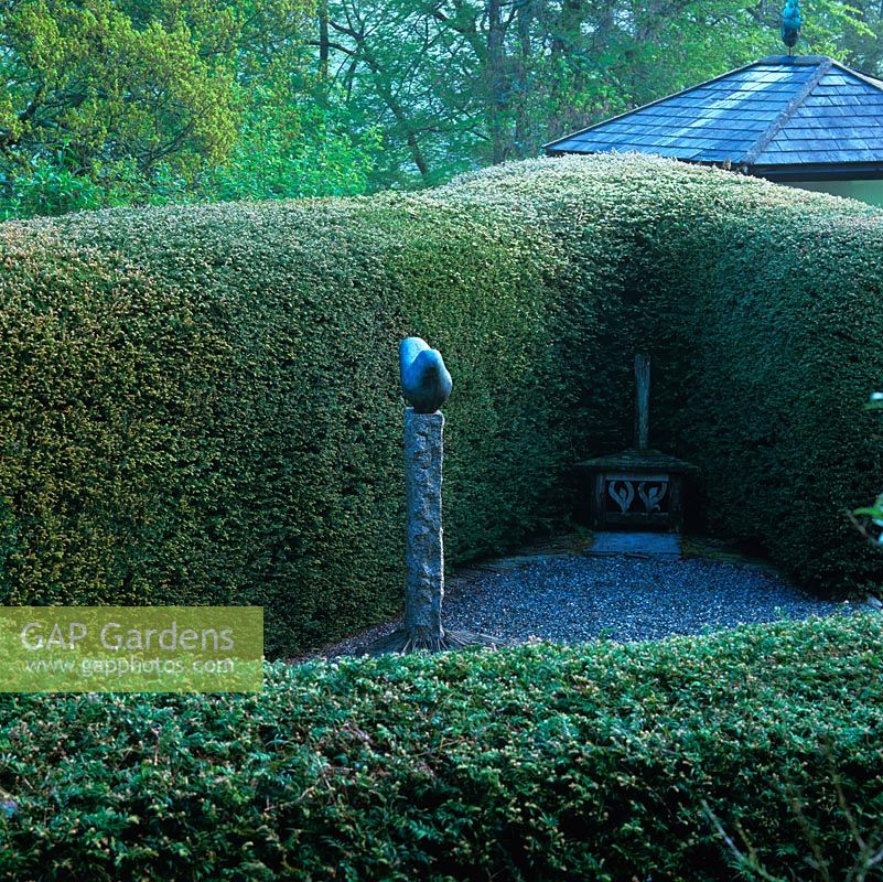 Triangle of rounded yew hedges encloses gravel courtyard.  'Cycladic Dove' sculpture by Bridget McCrum.
