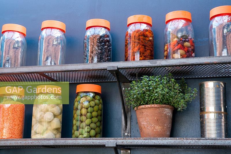 Shelves of jars of olives, pickles and a pot of thyme.