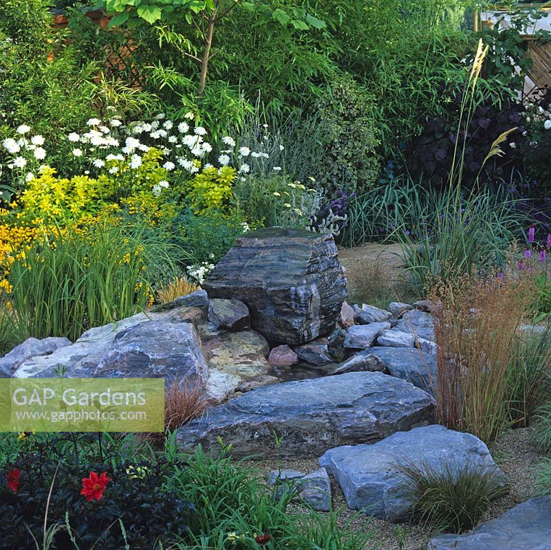 Great boulders are set at the heart of this garden, softened by grasses. Bed of chrysanthemum, choisya, rue, santolina and tagetes.