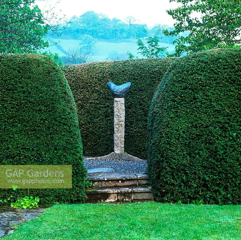 A triangle of tall, rounded yew hedges surround Bridget McCrum's 'Cycladic Dove', glimpsed through narrow gap.
