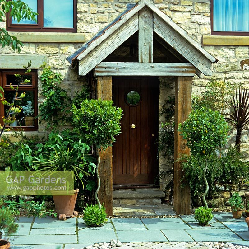 Stone and timber porch is flanked by two standard bay trees, trained over eight years up canes to created spiralling stems.