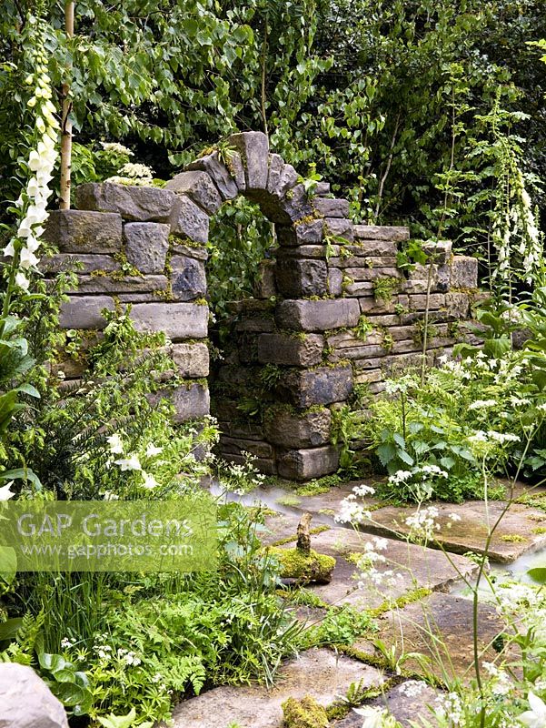 Natural stone arch in folly set in woodland. Native ferns and mosses fill fissures in wall, whilst foxgloves and cow parsley reach for light.