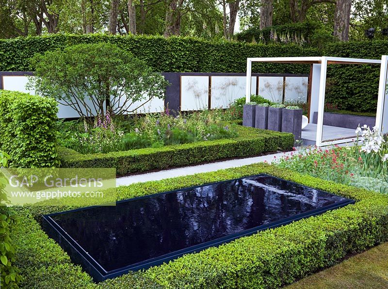 Pergola-like wooden frames focus attention on views within the space. Geometric layout of box and hornbeam mixes with perennials and shrubs. Rectangular pool framed in box.