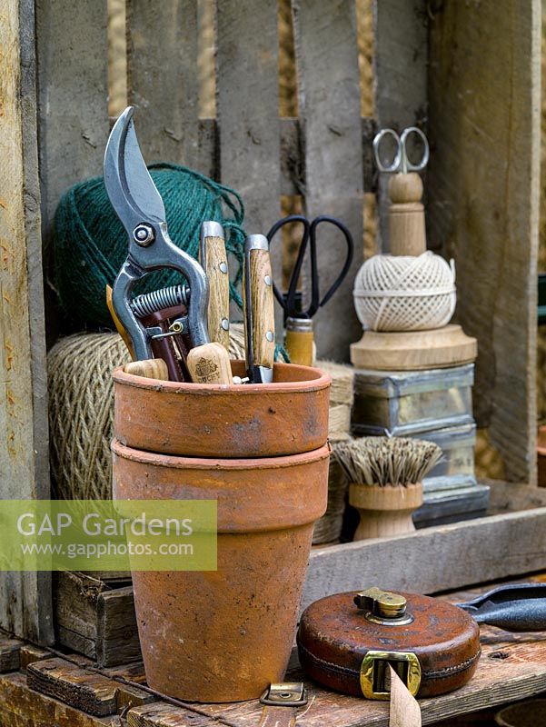 In corner of greenhouse, terracotta pots with secateurs, tape measure, balls of string and scissors.