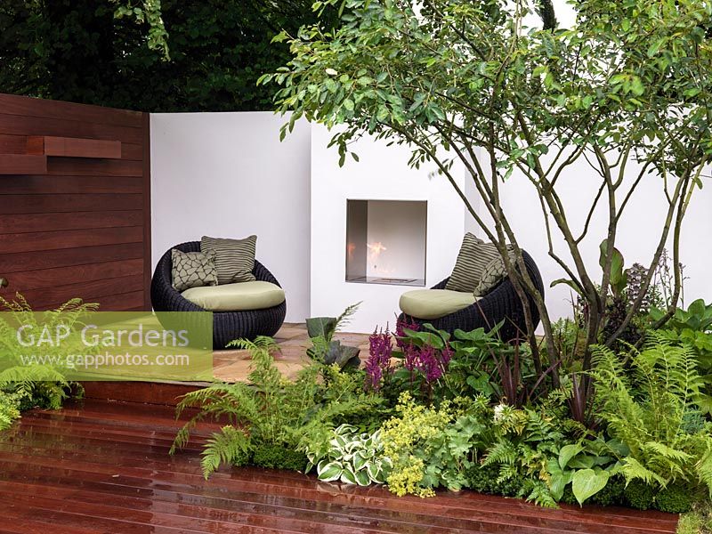 City courtyard with fireplace to bring warmth, light and a focal point. Beds of easy-care plants - ferns, hostas, alchemilla and astilbe.