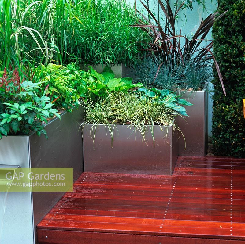 Urban courtyard retreat, with modern steel planters, smooth decking, oak table and seat, stainless steel planters with tranquil planting to add height, splashing waterfall and rill.