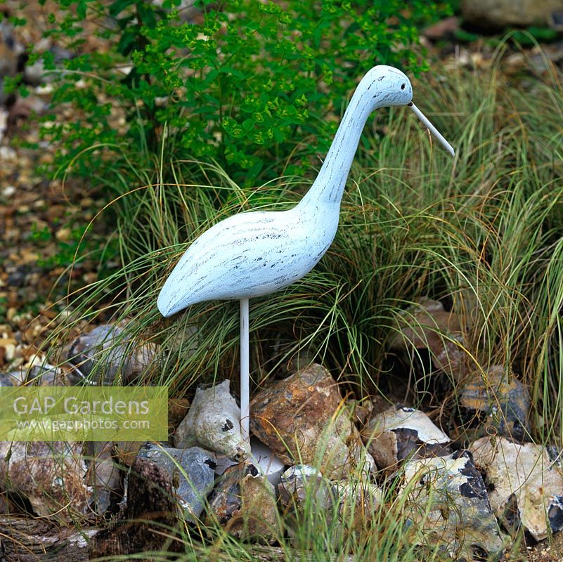Wooden model of sea bird stands among flints, euphorbia and grass - Carex comans 'Frosted Curls'