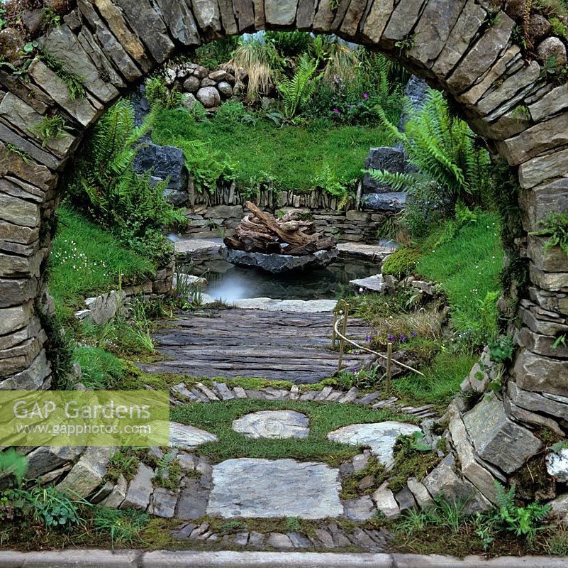 Glimpsed through a circular, dry stone window, a tranquil, personal sanctuary, naturalistic in style, with pool and seats.