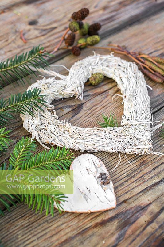 A white heart on a wooden surface, accompanied with a Birch heart, Pine foliage, Alder cones and Catkins
