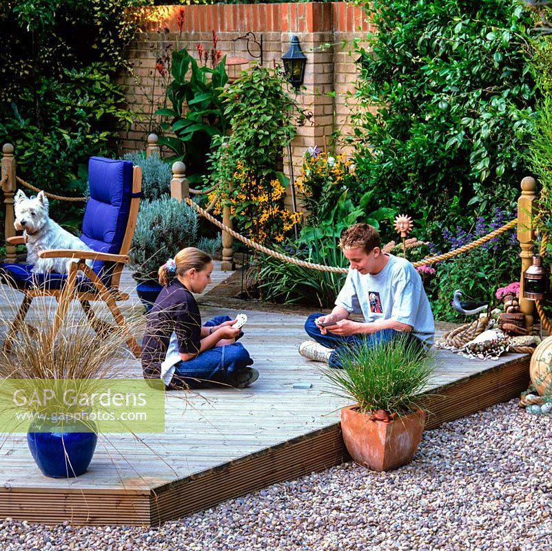 Siblings play cards on wood deck. Seaside-themed with grasses, pebbles, shells, model birds, rope and marine paraphernalia.