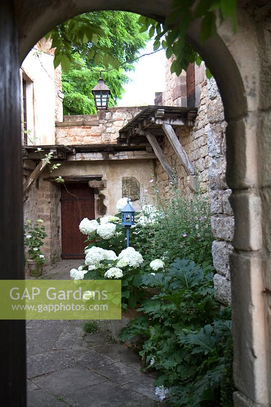 Courtyard garden with stone arch at Domaine de Chatelus de Vialar.  Hydrangea aborescens 'Annabelle' in terracotta pot.