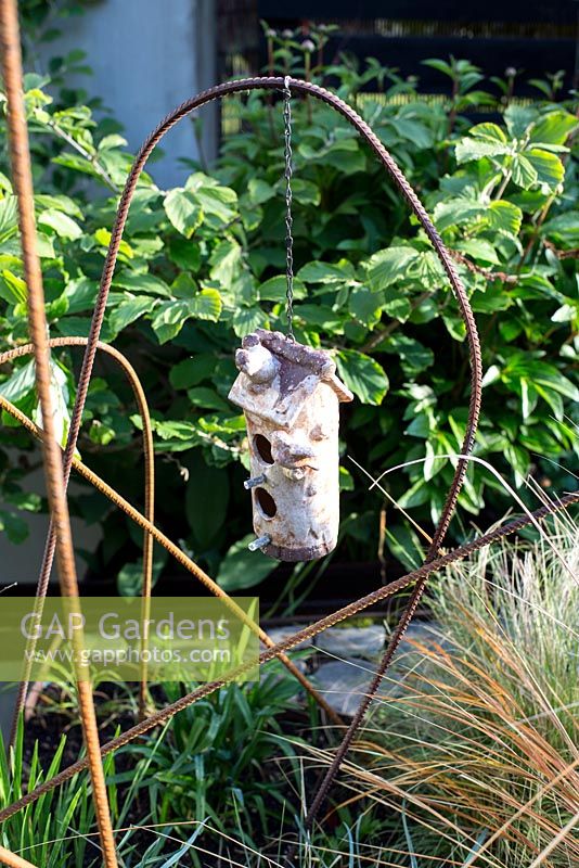 Ceramic bird box suspended on building rail plant support in town garden, Brixton