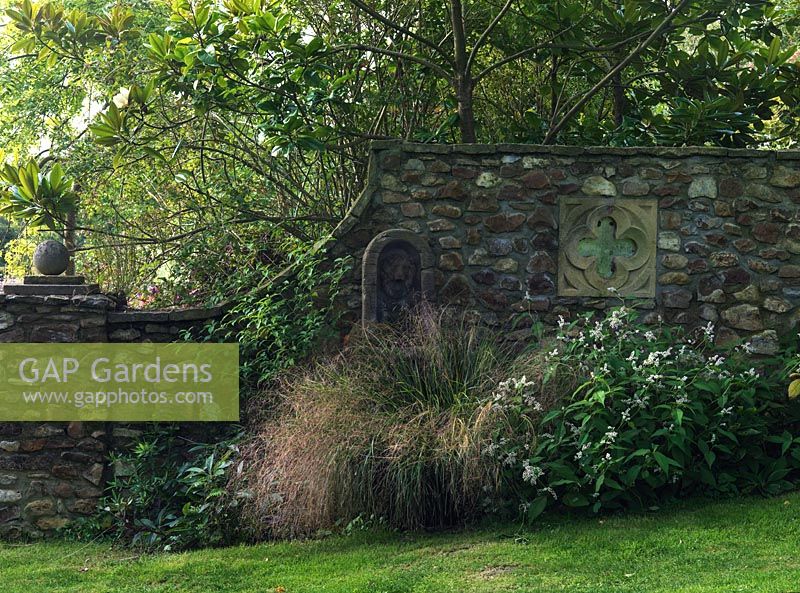 Wall built by John Hawkins from local stone with inset lion mask water spout. In the bed Stipa arundinacea is planted with white flowered Persicaria campanulata Alba Group.
