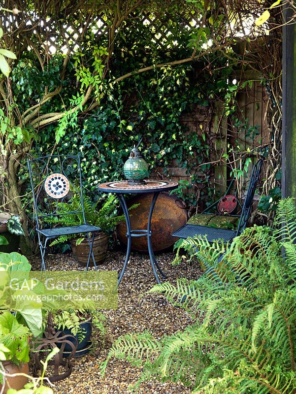 A seating area in a shady corner surrounded by ivy and ferns in containers.