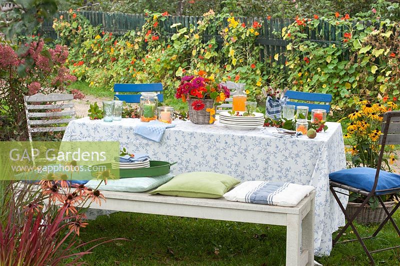 A garden table laid for a meal with a bouquet of zinnias and nasturtiums with branches of apples and blackberries for decoration
